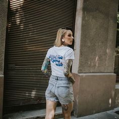 a woman walking down the street with tattoos on her arm and leg, wearing shorts