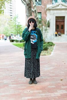 a woman standing in front of a tree while wearing a green jacket and black skirt