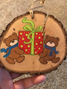 a hand holding a wooden ornament with two teddy bears and a present on it