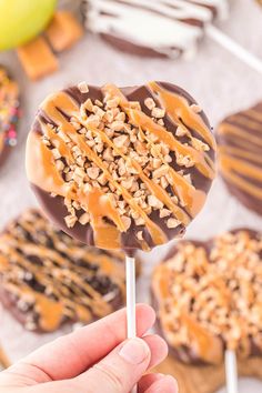 a hand holding a chocolate covered pretzel lollipop with caramel drizzle