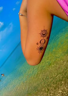 a woman's arm with the sun and moon tattoo on her left side, next to the ocean