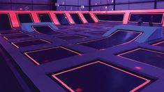 an indoor trampoline park with people walking around it and neon lights on the walls