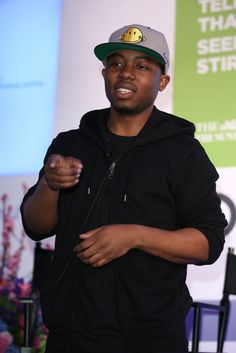 a man standing in front of a screen wearing a hat and holding his hands together