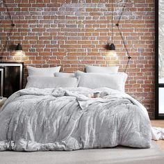 a bed with white sheets and pillows in front of a brick wall