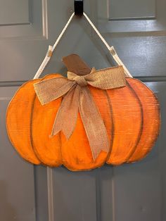 an orange pumpkin hanging from a door with a bow on it's front end