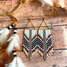 two pairs of earrings with beads and feathers hanging from them on a wooden table next to dried leaves