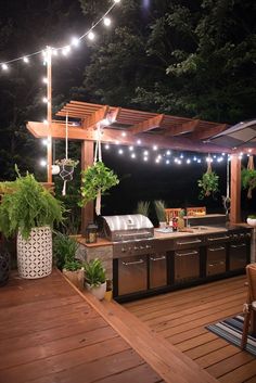 an outdoor kitchen is lit up with string lights and potted plants on the deck