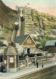 an old photo of a train going up the tracks near a mountain side town with people standing on it