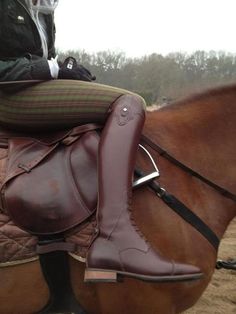 a person riding on the back of a brown horse wearing boots and sitting on top of it