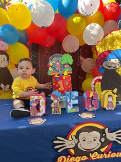 a baby sitting in front of a table with balloons and decorations on it, next to a sign that says diego curious