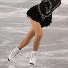 a female figure skating on the ice in a black dress and white sneakers with her arms outstretched