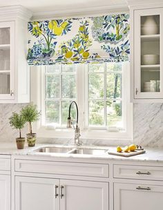 a kitchen with white cabinets and marble counter tops, yellow flowers on the window valance