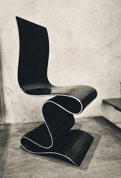 a black chair sitting on top of a wooden floor next to a white wall and stairs