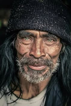 an old man with long black hair and a beard wearing a beanie on top of his head