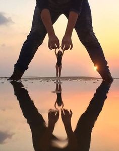 a man bending over to pick up something from the water with his reflection in the water