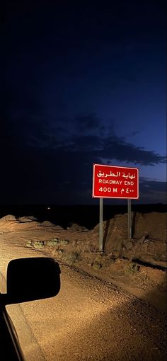 a red sign sitting on the side of a road next to a dirt field at night