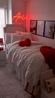 a bedroom with white bedding, red pillows and pictures on the wall above it