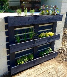 a wooden planter filled with plants next to a white brick wall and cement block