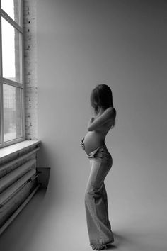 a pregnant woman leaning against a wall next to a window