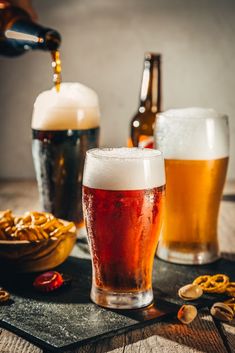 beer being poured into two glasses with pretzels on the table next to them