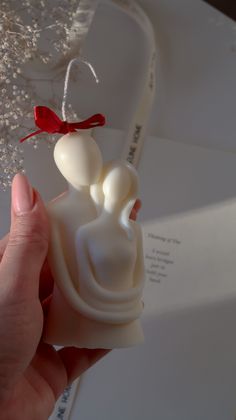 a hand holding a small white object in it's right hand, with a red bow on top