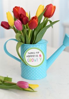 a watering can filled with tulips on top of a white table next to flowers