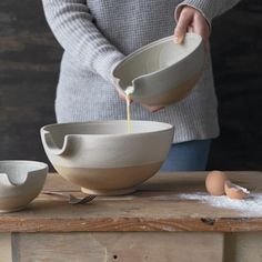 a person pouring something into a bowl on top of a wooden table next to two bowls