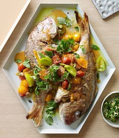 a white plate topped with fish covered in veggies and sauce next to a bowl of salad