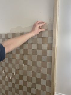 a woman is pointing at the wall with her hand on it, in front of a tiled wall