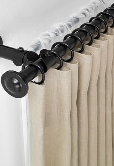 the curtain rod is attached to the side of a window with black metal rods and white curtains