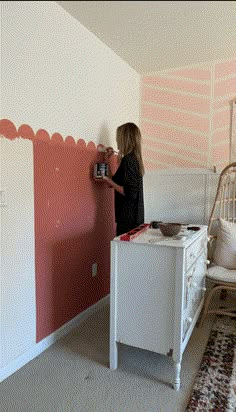 a woman is painting the wall in her bedroom with pink and white stripes on it