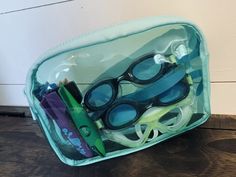 a clear bag filled with swimming goggles and other items on top of a wooden table