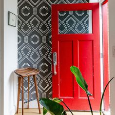 a bright red door in front of a black and white wallpaper with a wooden stool next to it