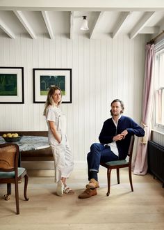 a man and woman sitting at a table in a white room with wood flooring