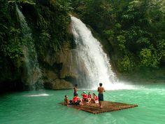 people are standing on a raft in the water near a waterfall