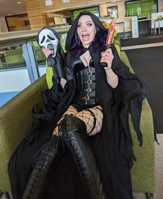 a woman sitting on a green couch holding two halloween items in her hands and wearing a black outfit