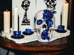 a white skull with blue flowers on its head and candles in front of it sitting on a table