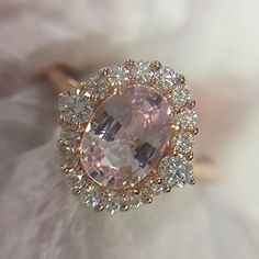 an oval shaped pink diamond surrounded by smaller round diamonds on top of a white flower