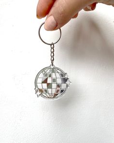 a hand holding a metal keychain with a globe on the front and bottom