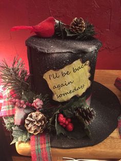 a black hat with writing on it and pine cones around the top, sitting on a wooden table