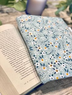 an open book sitting on top of a wooden table next to a vase filled with flowers