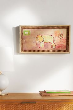 an elephant painting hangs on the wall above a dresser with a lamp and bookcase