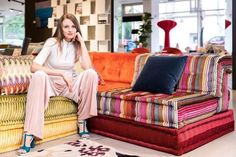 a woman sitting on top of a multicolored couch in a room filled with furniture