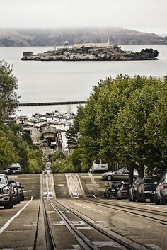 cars are parked on the side of train tracks next to an island in the distance