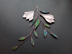 a metal brooch with green and white leaves hanging from it's side on a black surface