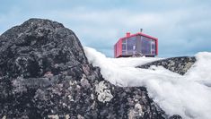 a small red house sitting on top of a large rock covered in snow and ice