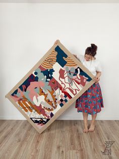 a woman standing next to a large piece of art on a wooden floor in front of a white wall