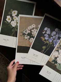 three pictures of flowers are being held by a woman's hand on top of a table