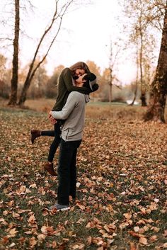 a woman holding a child in her arms while walking through leaves on the ground and trees