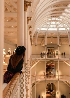 a woman standing on the balcony of a building looking down at people in the atrium